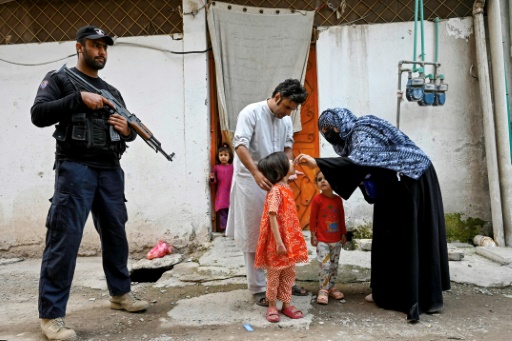 Un policier monte la garde pendant qu'une agente de santé (d) administre un vaccins contre la polio à un enfant lors d'une campagne en porte-à-porte, à la périphérie de Peshawar, le 29 octobre 2024 au Pakistan
