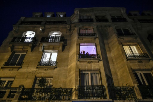 Des personnes se tiennent à leur fenêtre pendant les applaudissements quotidiens de 8 heures en soutien aux soignants, le 27 mars 2020 à Paris, au onzième jour d'un confinement visant à freiner la propagation du Covid-19 en France
