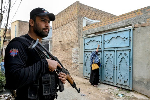 Un policier monte la garde pendant qu'une agente de santé va de maison en maison pour vacciner les enfants contre la polio, à la périphérie de Peshawar, le 29 octobre 2024 au Pakistan
