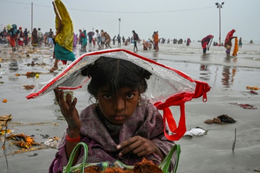 Une enfant se protège de la pluie avec un sac en plastique sur pendant le festival hindou Gangasagar Mela, le 14 janvier 2022 en Inde
