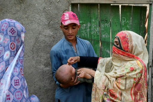 Une agente de santé administre à un enfant un vaccin contre la polio lors d'une campagne en porte-à-porte, à la périphérie de Peshawar, le 5 octobre 2024 au Pakistan
