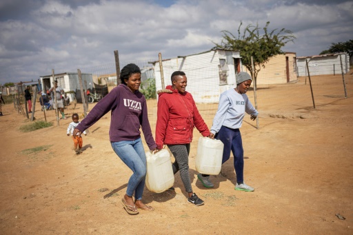 Trois femmes transportent des bidons remplis d'eau à Hammanskraal, en Afrique du Sud, le 23 mai 2023
